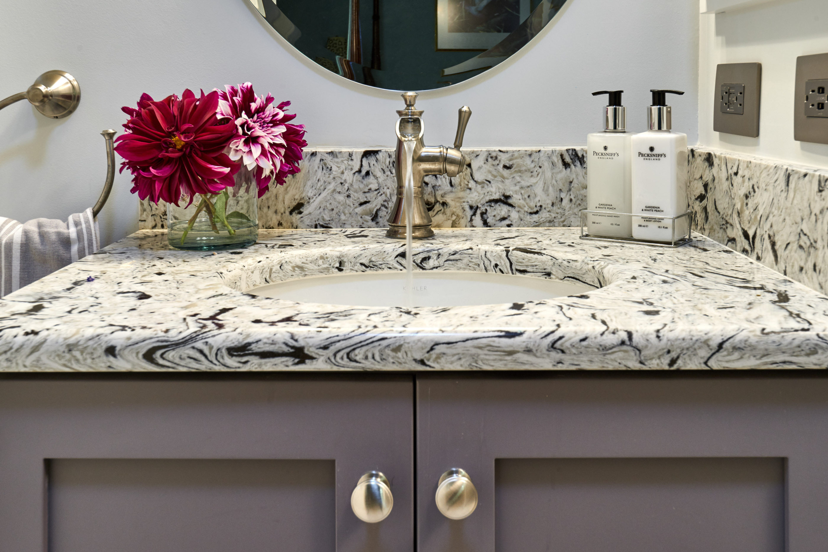 quartz countertop sits on custom gray vanity cabinets with brushed nickle waterfall faucet 