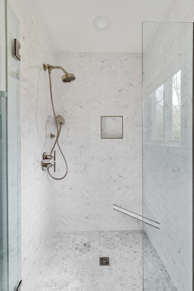 White tiled shower with frameless, glass enclosure and corner bench