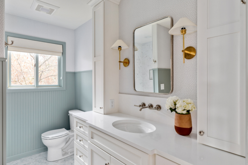 Bathroom with blue wainscoting, white cabinets and countertops, and wall mounted lights