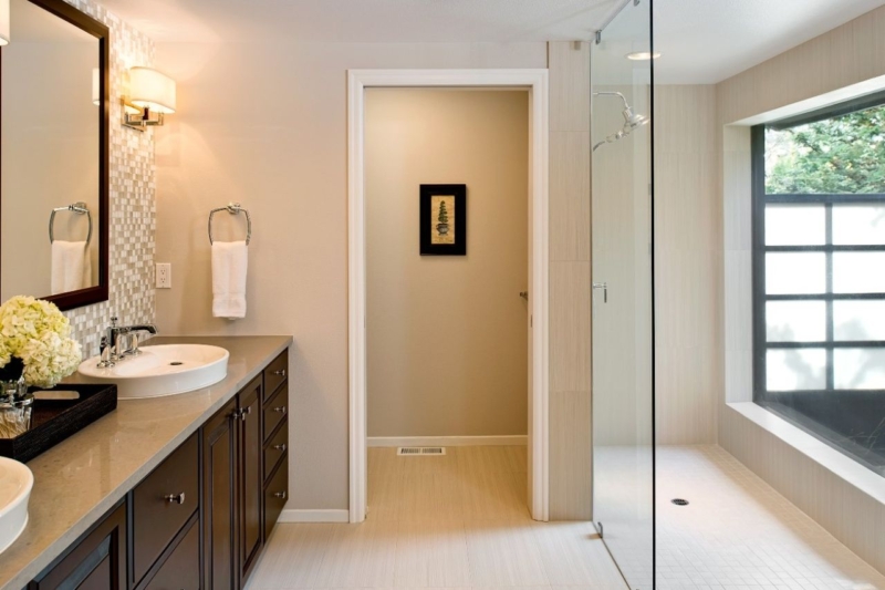 A floor-to-ceiling glass wall allows natural light to fill the remodeled master bathroom.
