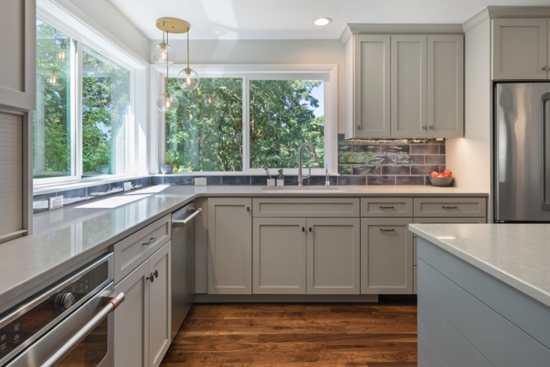 Light gray cabinetry and stainless appliance are contrasted with brass lighting fixtures Light gray cabinetry and stainless appliance are contrasted with brass lighting fixtures