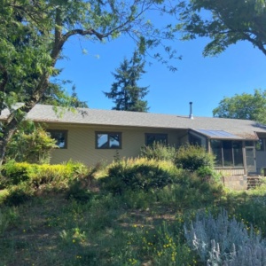 Before 1980's ranch style home amid landscape of mature trees and brush, before addition and remodel by Powell Construction.