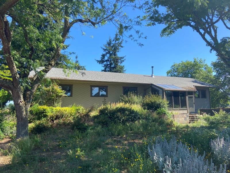 1980's ranch style home amid landscape of mature trees and brush, before addition and remodel by Powell Construction.