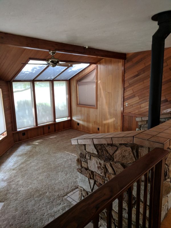 Dark sunken living room prior to remodel, featuring wood paneled walls and a woodburning stove.