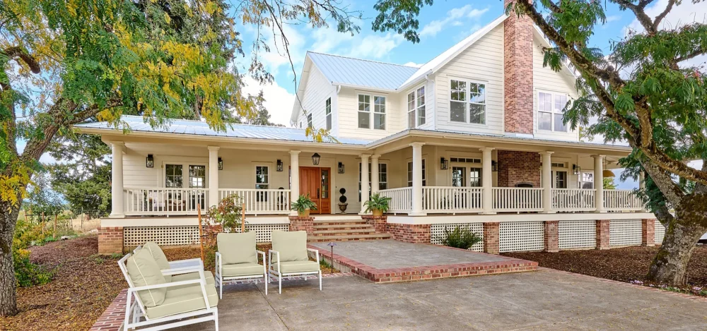 Exterior view of traditional southern farmhouse, gracious wrap-around porch and columns.