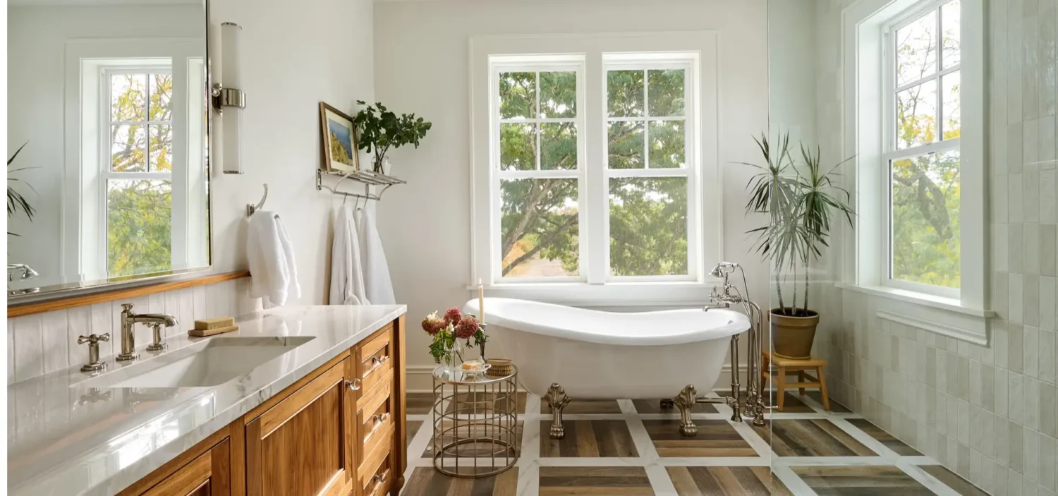 Bright and elegant bathroom with a freestanding clawfoot tub positioned in front of large windows, allowing natural light to flood the space.