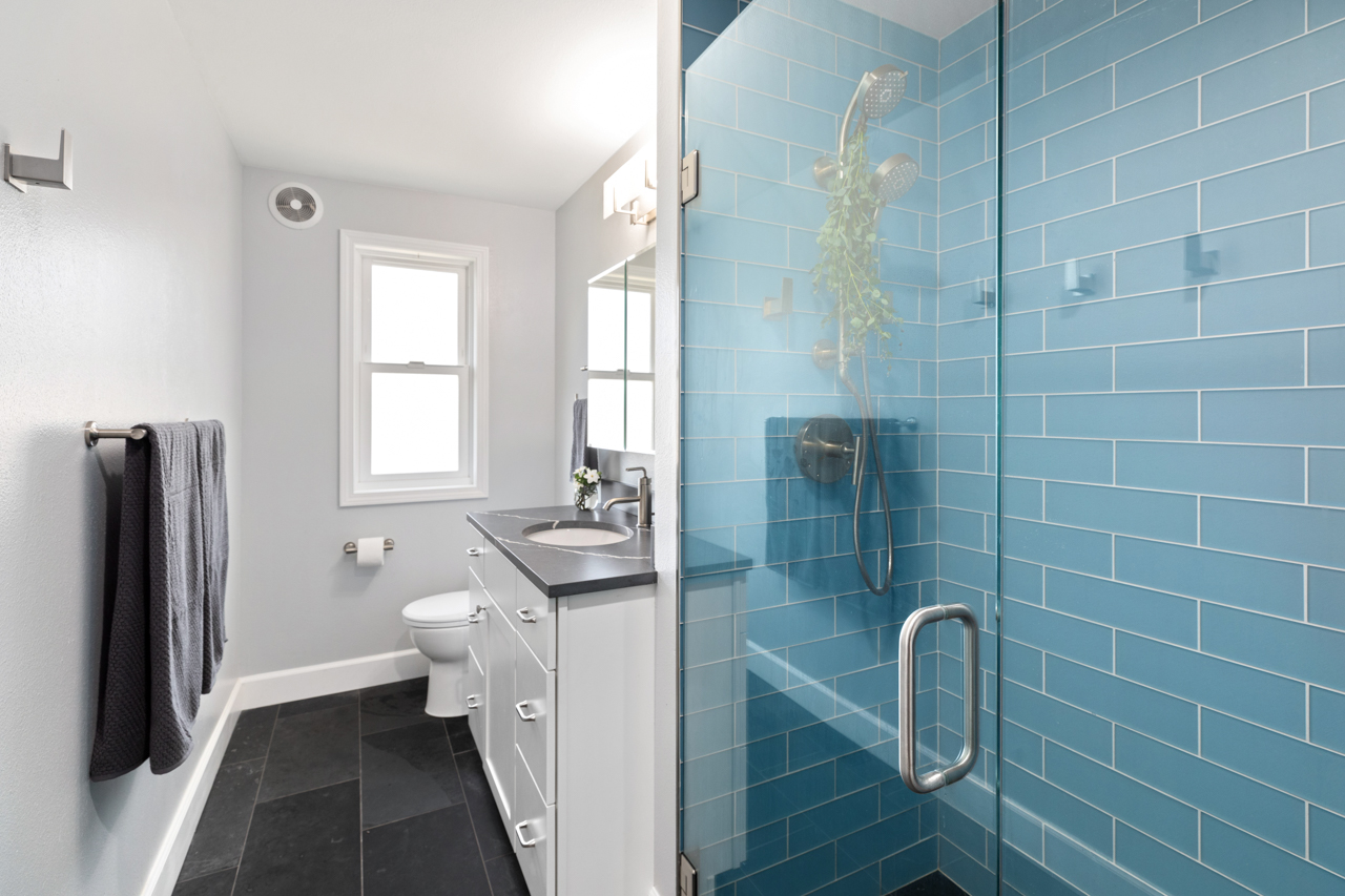 Contemporary, remodeled bathroom with blue glass tile in the shower and black slate tile for the flooring. With all other elements white, this is a bright, refreshing space.