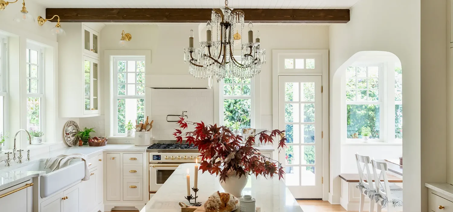 English Cottage style kitchen addition with warm white cabinetry, rough hewn beams, and white quartz countertops.