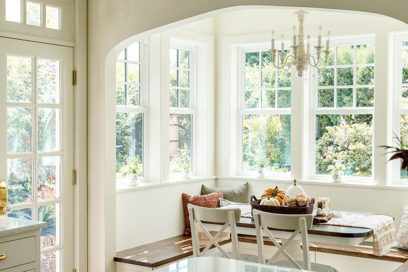 Cozy breakfast area featuring a banquette seating, white wood chandelier, and multiple windows overlooking the garden.