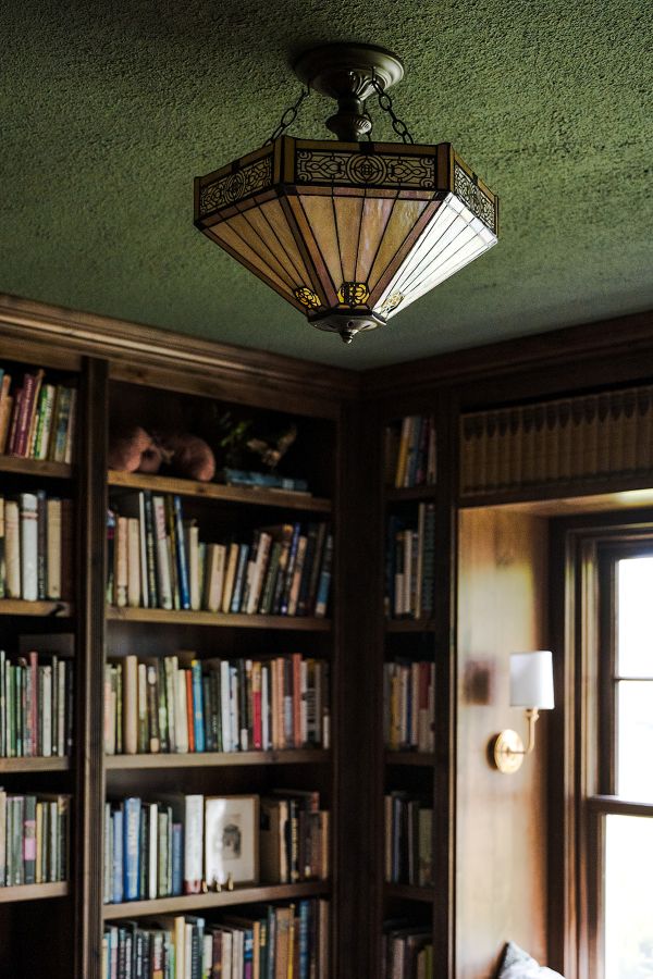 Study with custom built-in bookcases, green ceiling, window bringing in natural light, and decorative semi-flush ceiling light fixture.