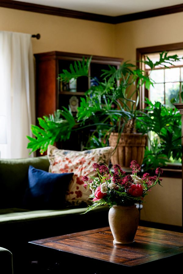 Living room with a coffee table centerpiece of florals and greenery in focus, with wooden bookshelves visible beyond.