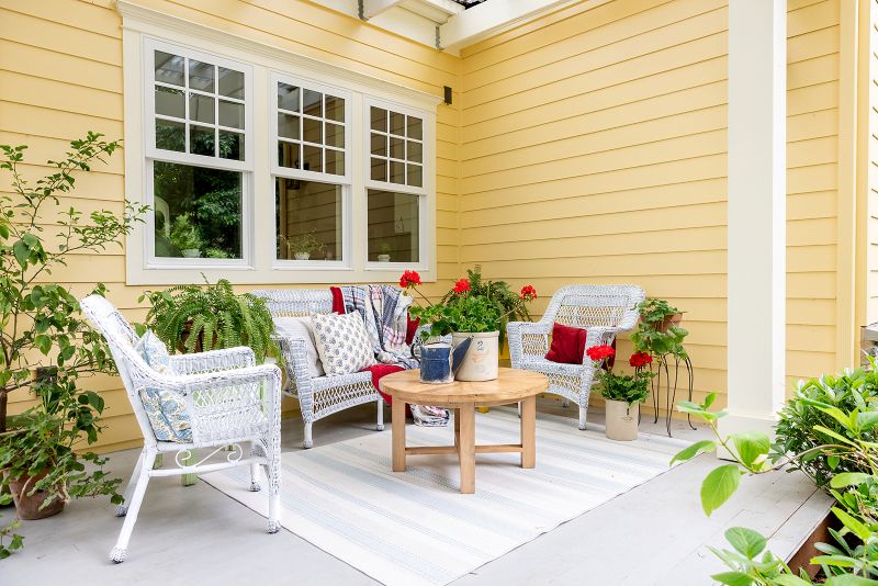 Covered porch with seating area includes rug, wicker furniture and wooden coffee table.
