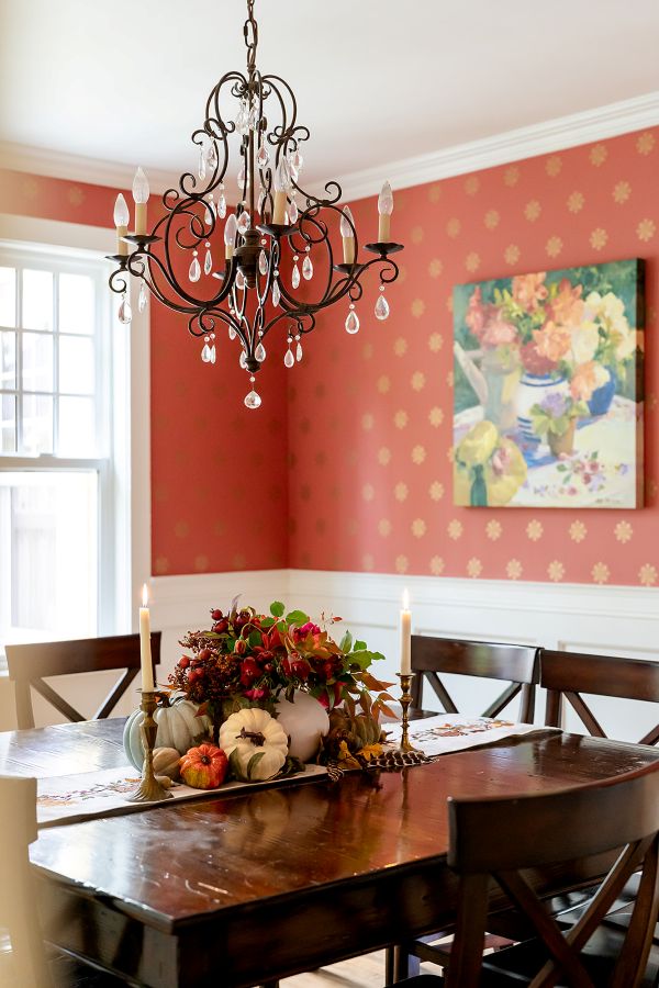 Crystal chandelier with beautiful coral and gold wallpaper and wainscotting in background.