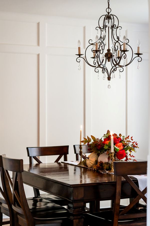 Chandelier hangs over a wooden dining table with historic, white wall paneling as backdrop.