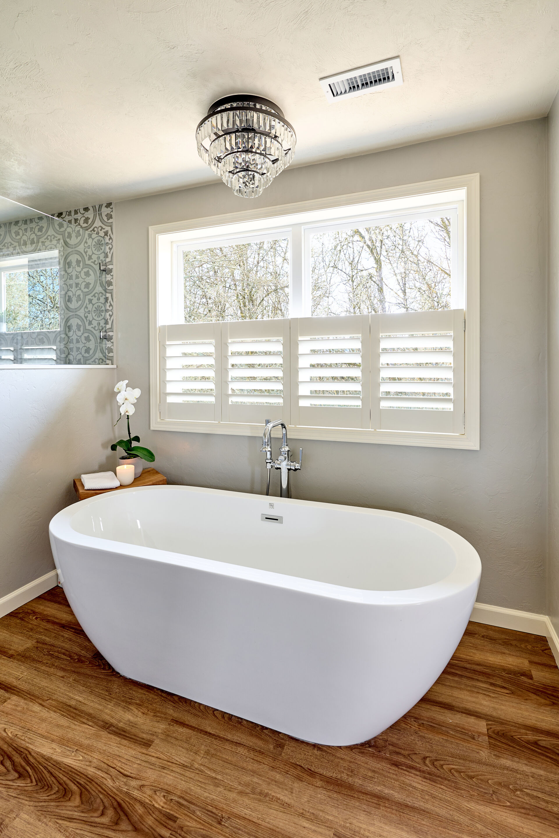 Vertical photo of freestanding tub on wood-look LVP flororing with a semi-flush chandelier hanging above.