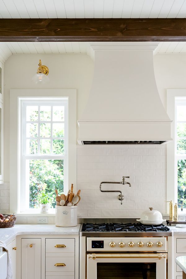 Elegant kitchen setup with a cream Ilve range, brass knobs, and a custom wood hood in soft white.