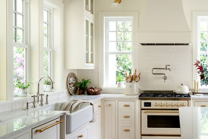 Corner view of a kitchen with natural light streaming through a window, highlighting glass-front cabinets.