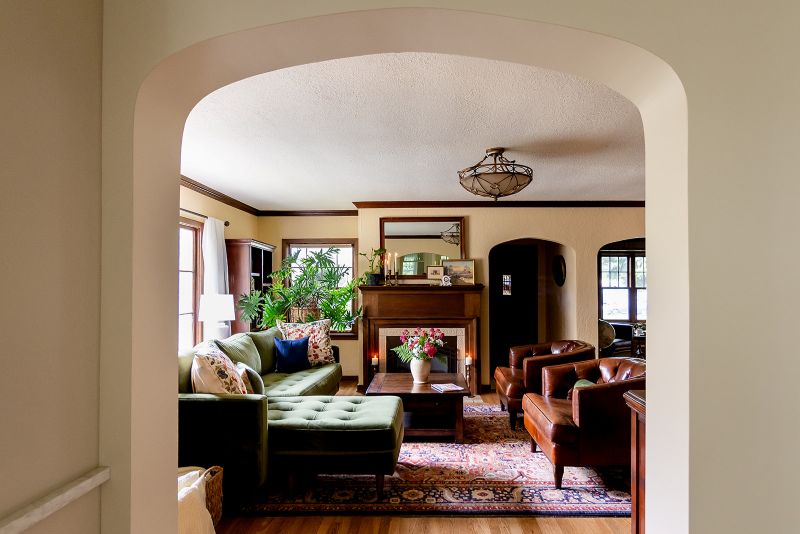 View from kitchen through arched entry into living room with custom wood mantle, detailed trim and moldings around fireplace.