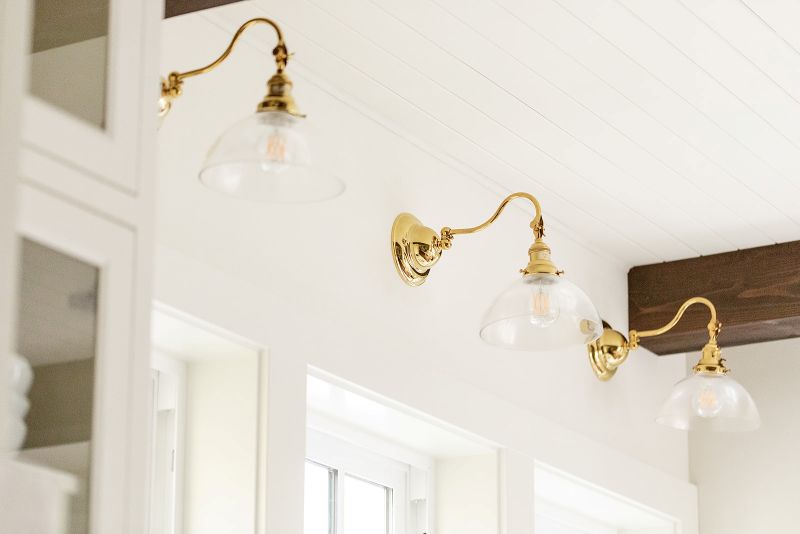 Three glass shades on brass, gooseneck wall sconces hang over the kitchen windows