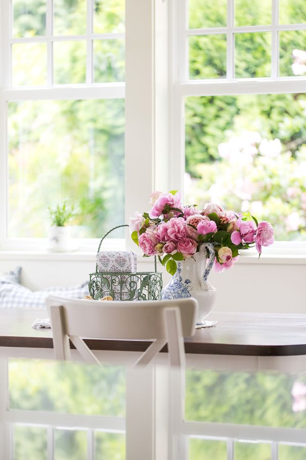 Detail view of bright pink rose bouquet in white and blue vase on breakfast nook table