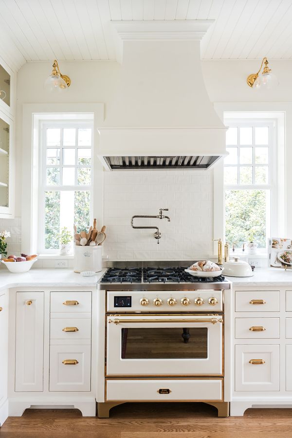 Creamy white Ilve range with custom wood hood above, flanked by gridded windows.