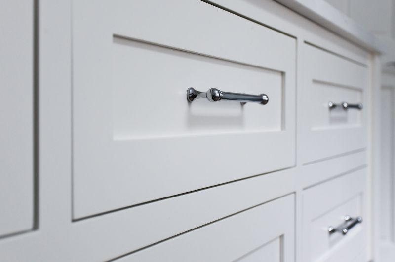 Polished chrome cabinet pulls installed on white cabinet drawers.