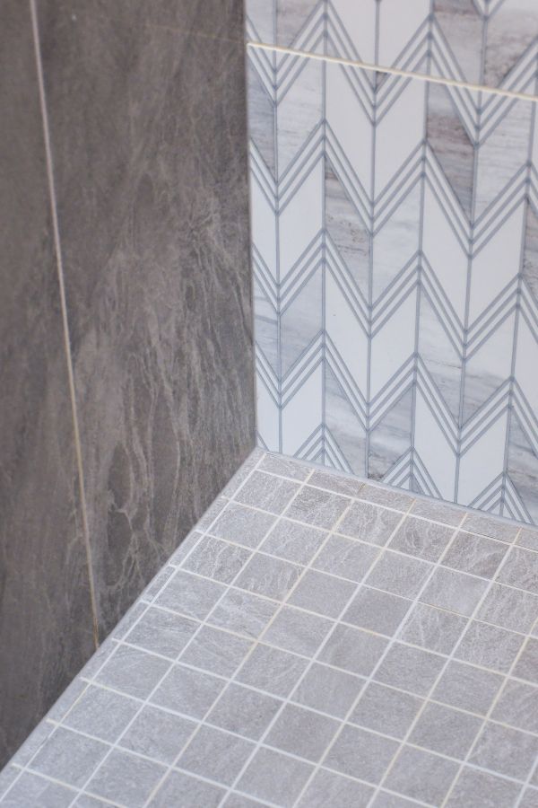 Detail photo of wall tile and floor tile in shower. A combination of large format, smaller square floor tile and a wall accent of chevron patterned tile.