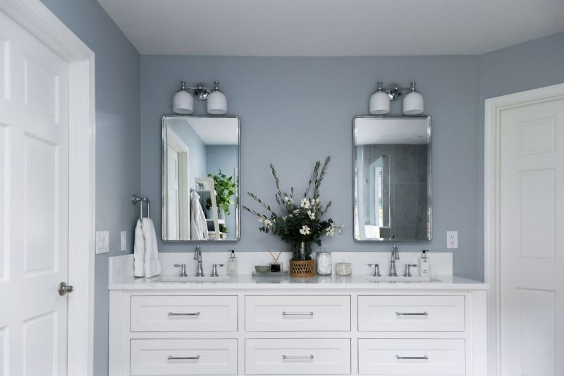 Photo of white double vanity with polished chrome fixtures and mirrors and light blue gray walls.