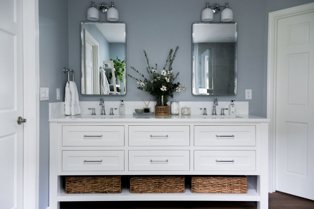 Photo of white double vanity with polished chrome fixtures and mirrors and light blue gray walls.