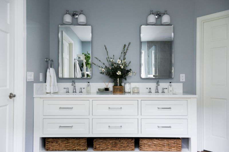 Photo of white double vanity with polished chrome fixtures and mirrors and light blue gray walls.