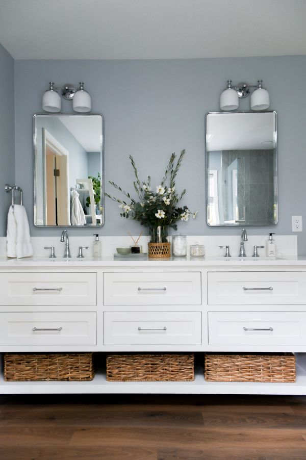 Vertical photo of white vanity with double sinks and storage baskets below.