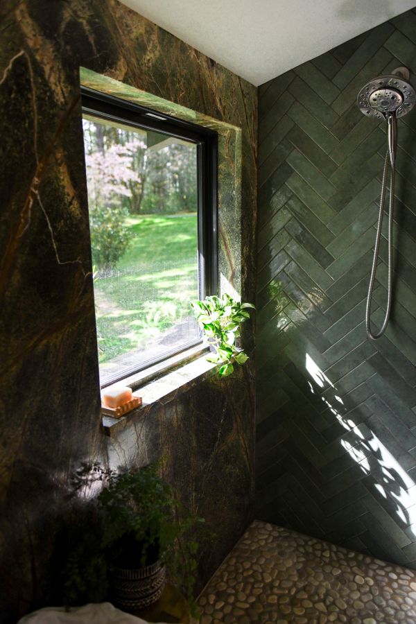 Corner of shower showing window, rainforest marble and tile wall with herringbone pattern.