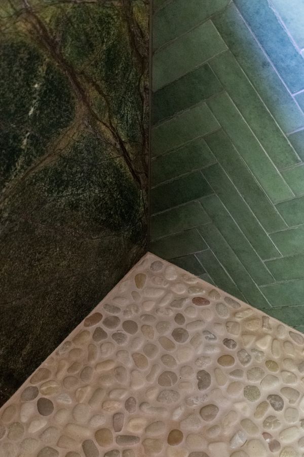 Photo detailing mosaic pebble flower, herringbone tile wall, and marble wall--all coming together in the corner.